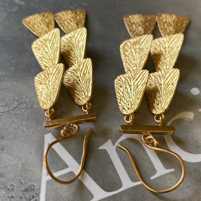 Pair of gold dangle earrings upside down on grey background.