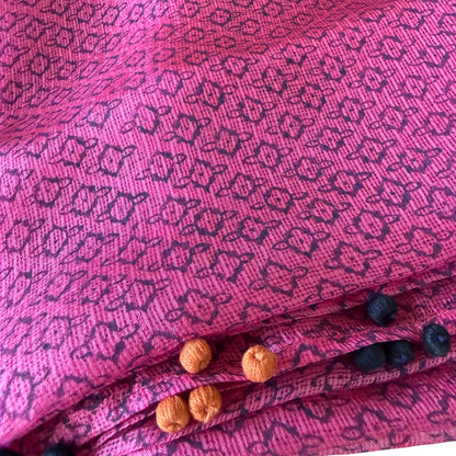 Close-up of a pink Kota silk scarf in rose magenta showing block-printed floral motifs, checkered weave and hand-knotted marigold and charcoal cotton tassels.
