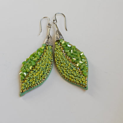 Pair of leaf shaped green glass bead earrings with silver findings on grey background.