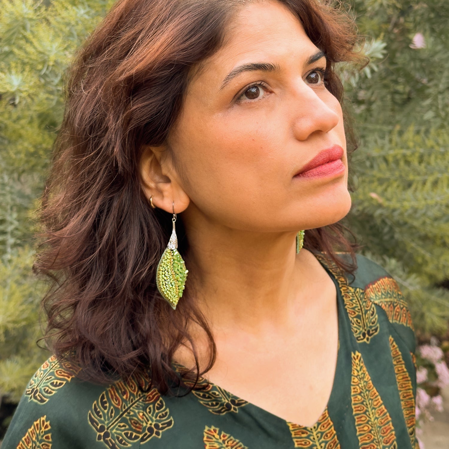 Right front view of woman wearing leaf shaped green glass bead earrings with gold findings.