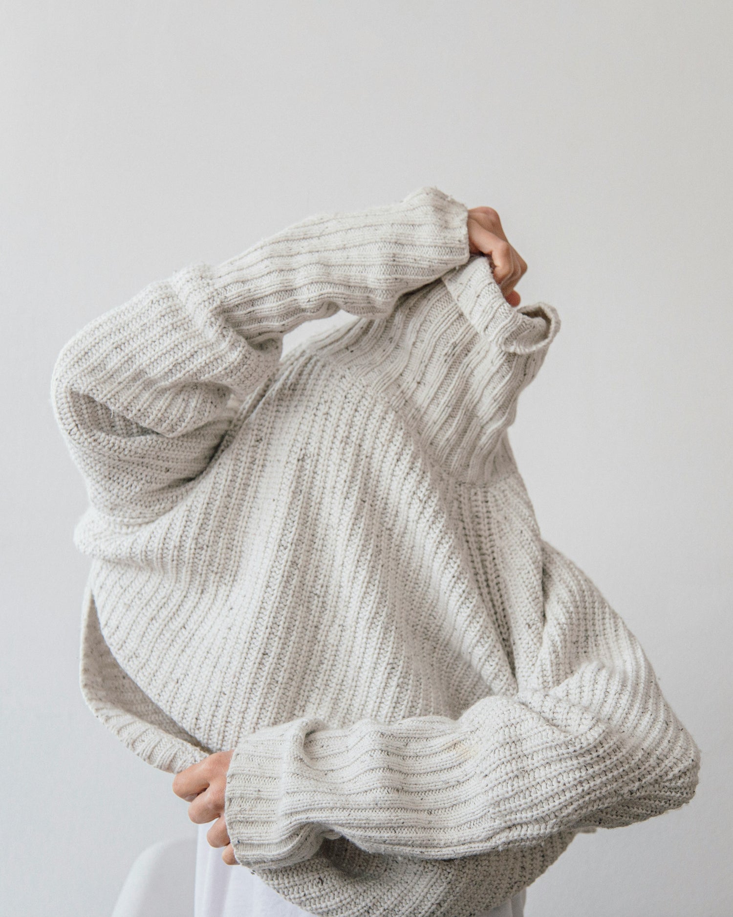 Person pulling white ribbed sweater up over their head.