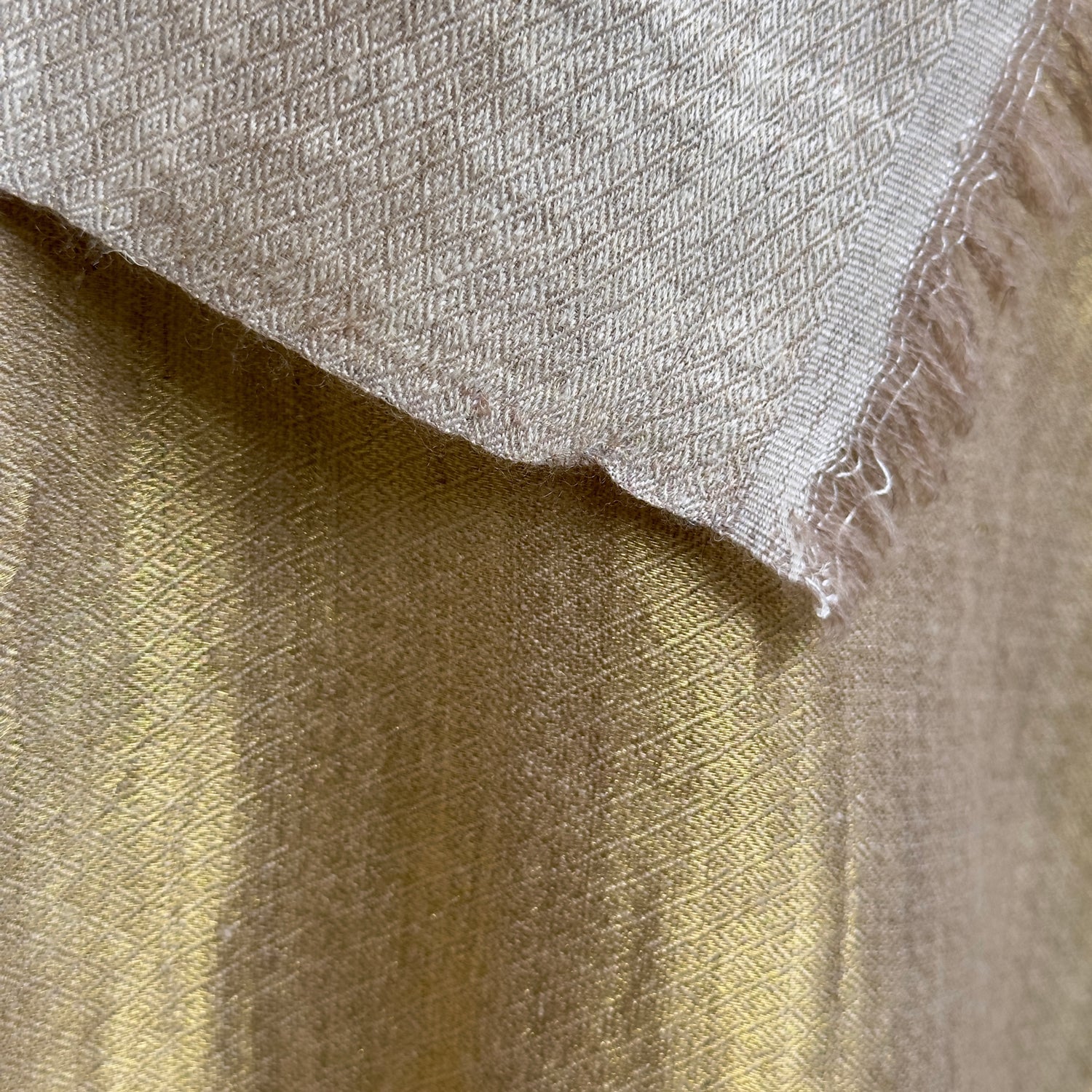 Closeup of gold material with taupe side visible at top.
