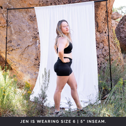 Side view of woman in front of a white sheet, wearing black toura short with 5" inseam.