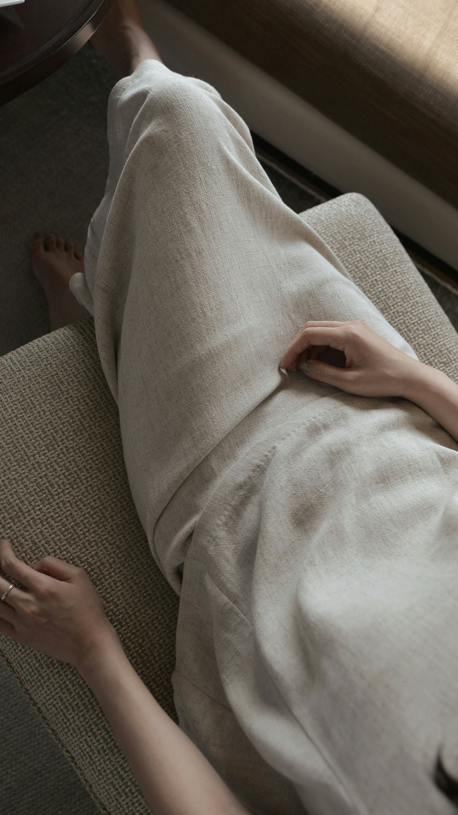 Downward view of a woman in natural linen skirt and top sitting with crossed legs.