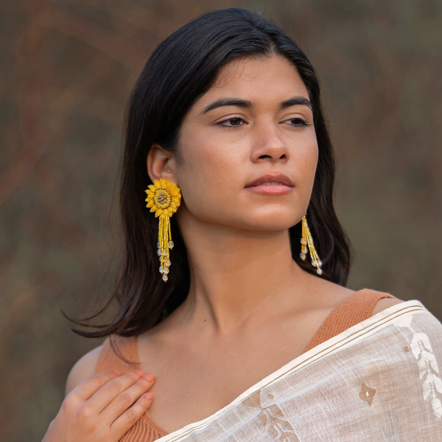 Front view of woman wearing pair of dahlia design earrings in red, yellow, green, and brown.
