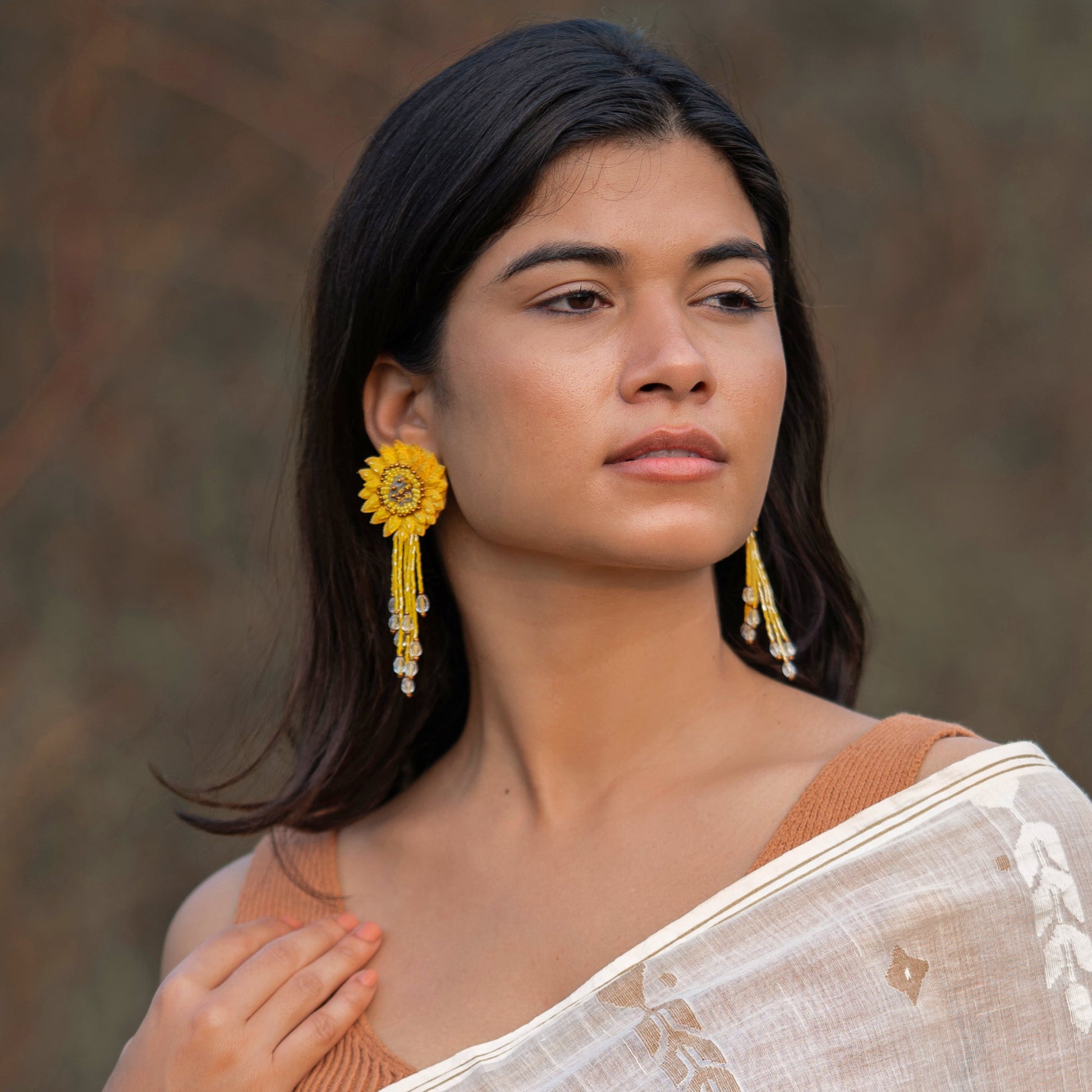 Front view of woman wearing pair of dahlia design earrings in red, yellow, green, and brown.