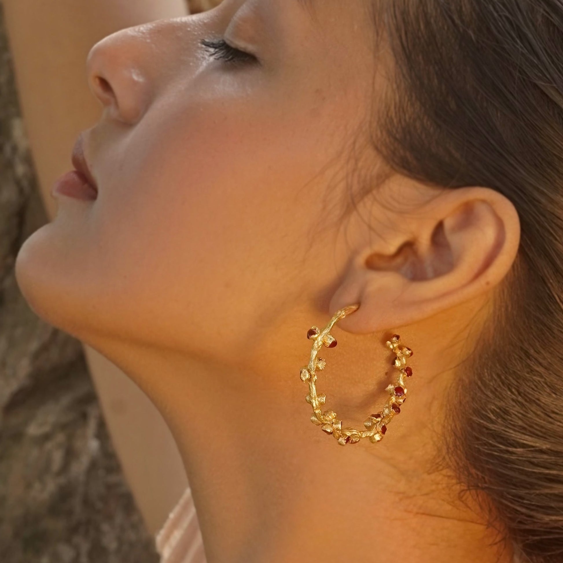Left front view of woman looking up wearing red and gold hoop earrings.