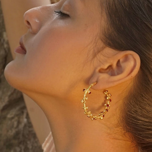Left front view of woman looking up wearing red and gold hoop earrings.